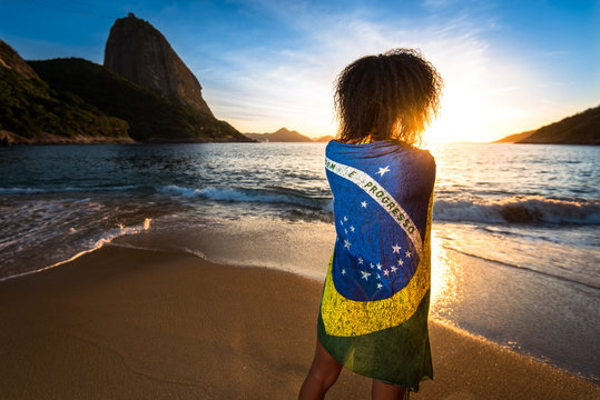 Girl With Curly Hair and Brazilian Flag on Her Back Standing in the Beach and Watching the Sunrise with the Sugarloaf Mountain in the Horizon, in Rio de Janeiro