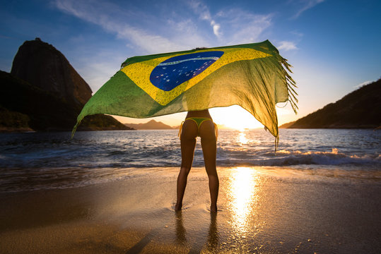 Sexy Girl in Bikini Holding Beach Yoke With Brazilian Flag Waving in the Wind, with the Sugarloaf Mountain View by Sunrise, in Rio de Janeiro