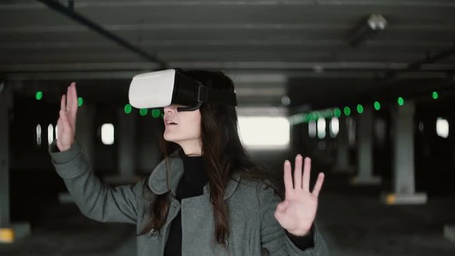 Young woman using a virtual reality glasses on parking place. Girl touching space with hand wearing VR headset. 4K