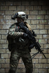 US Army Ranger with machinegun and night vision goggles standing near the wall. Side view profile