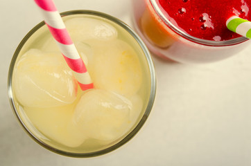 Strawberry smoothies and ice lemonade with cocktail tubes in glasses, on white background.