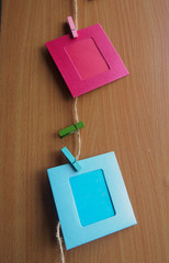 red and blue picture frame hanging on the ropes with the peg on wooden wall background