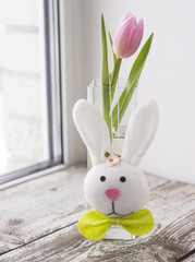 Pink tulip and Easter bunny toy on a shabby wooden table.