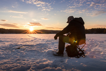 Ice fishing on a lake in Norway at sunset.