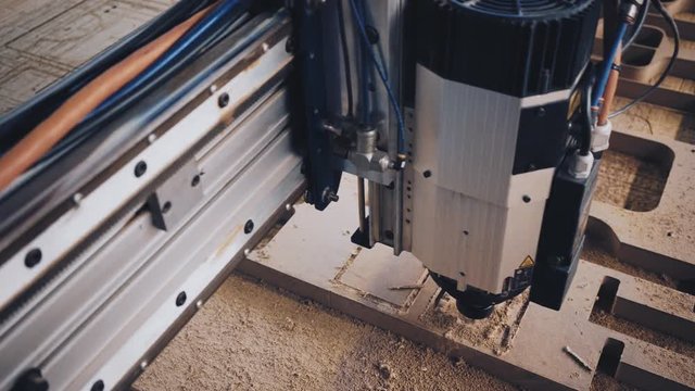 Top view on big industrial cut machine at work in wood worker manufacture. Drill cuts out rectangular shape mold from solid piece of compressed laminate. Small artisan business concept
