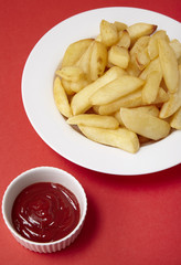 A bowl of French fries with tomato ketchup on a bright red background