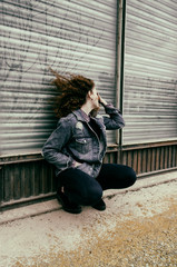 Chica joven con ropa urbana esperando apoyada en la pared de una fábrica cerrada 