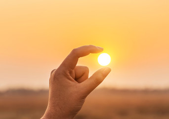Obraz premium Złap sylwetka trzymając słońce w palcach. Sylwetka łapie słońce przy zmierzchem w palcach