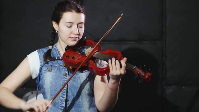 4k young girl playing the violin with her eyes closed, studio, black background