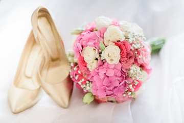 Pink wedding bouquet lies before golden shoes