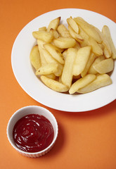 A bowl of French fries  and ketchup on a bright orange background