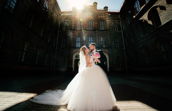 Bearded groom and bride in magnificent dress pose in rays of bright sun