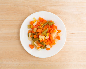 Top view of mixed vegetables on a white plate atop a wood table.
