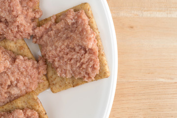 Top close view of deviled ham and crackers on a white plate atop a wood table.