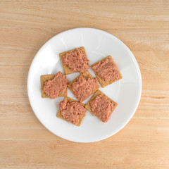 Top view of a plate of deviled ham on crackers atop a wood table.
