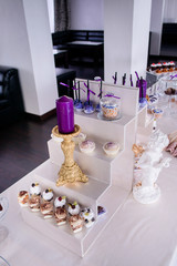 Violet candle on golden candleholder stands on white box with cupcakes and other sweets