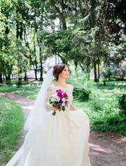 Fototapeta na wymiar Bride holds her magnificent dress walking in it around green park