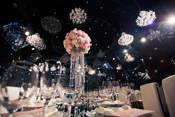 Tall centrepiece made of pink flowers and crystal chains stands under crystal chndeliers hanging from the ceiling