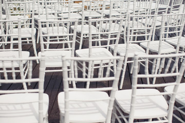 Elegant plastic white chairs stand in rows on grey wooden floor