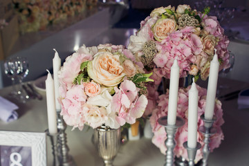 Tall white candles stand around little pink bouquets in silver vases