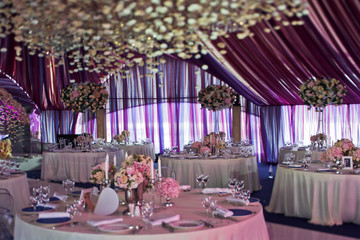 Round dinner tables stand under the violet tent prepared for wedding party