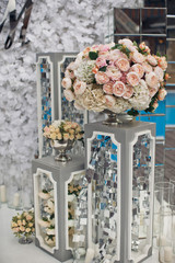 Large bouquet of pastel pink roses stands on grey box before white wedding altar
