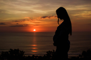Silhouette of pregnant woman. Side view of silhouette of pregnant woman standing on the background of sunset.