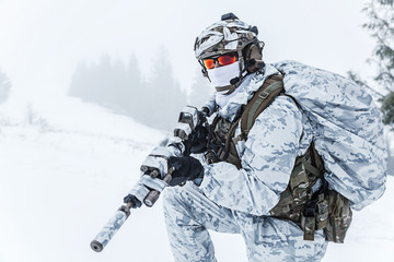 Winter arctic mountains warfare. Action in cold conditions. Trooper with weapons in forest somewhere above the Arctic Circle