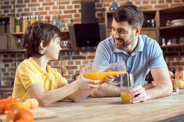 Happy father looking at little son pouring fresh juice in glass
