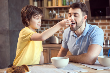 Cute smiling boy feeding father with breakfast