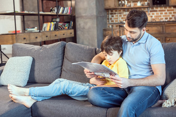 focused father and son reading newspaper together at home