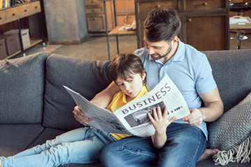 focused son reading newspaper to father at home