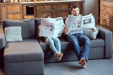 father and son sitting on couch and reading newspapers