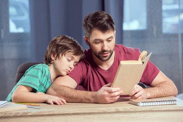 father reading book to sleeping son on shoulder