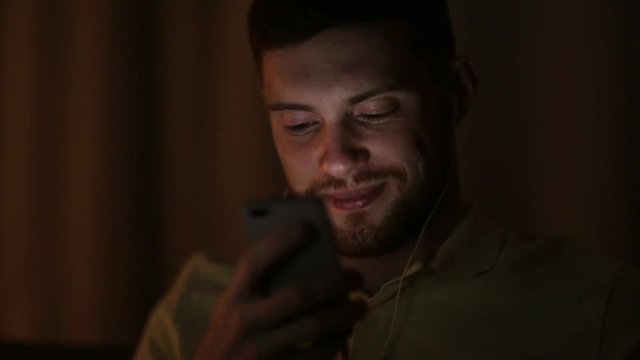 man with smartphone and earphones at night