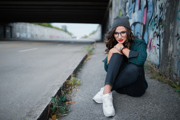 Thoughtful girl sitting on an empty highway under the bridge and thinks
