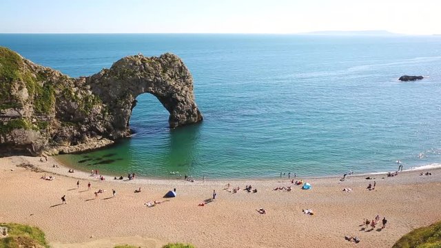 Aerial view of beach and rocks in Dorset county, England, UK. People sunbathing and swimming in the clear water. The limestone arch is called Durdle Door.