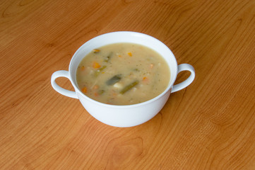 Vegetable soup in a white bowl on wooden background.