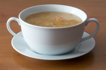 Polish cabbage soup in a white bowl on wooden background. Soup knows in Poland as Kapusniak.