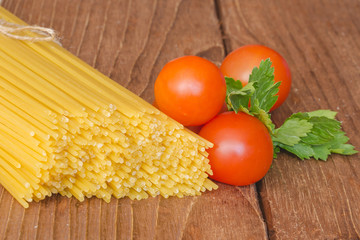 На столе лежат спагетти с помидорами и зеленью.