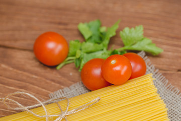 На столе лежат спагетти с помидорами и зеленью.