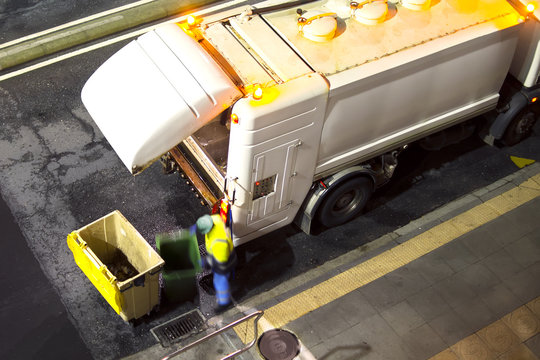 Utility Worker Of Service Company In Truck  For Cleaning The Dumpsters Containers At  Night