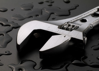 adjustable wrench on wet black background with water drops, macro