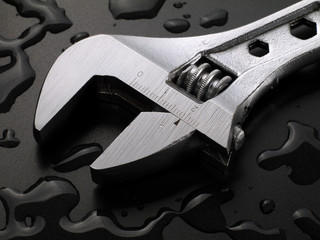 adjustable wrench on wet black background with water drops, macro
