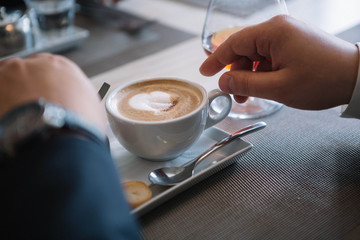 Fototapeta na wymiar Man's hand holding a white cup of coffee with milk