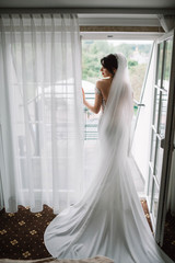 beautiful and young bride in white dress standing near window