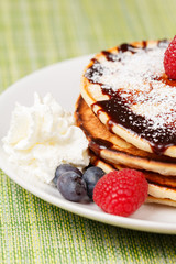 Pile of Pancakes with blueberries and raspberries, chocolate sauce and powder sugar