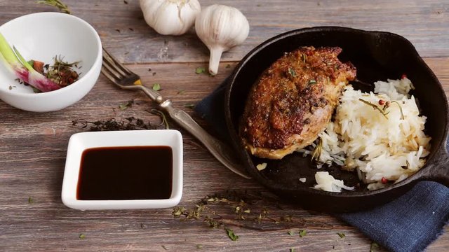 Roasted duck meat on cast iron pan, rice, soy sauce, spices, garlic bulbs on wooden table. Slow pan. Top view.