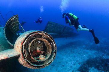 SCUBA divers explore the engine area of an underwater plane wreck