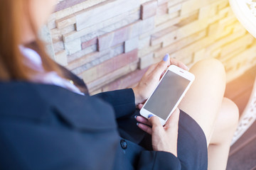 Close-up of female hands using modern smart phone while working at office with computer, businesswoman typing text message on her cellphone